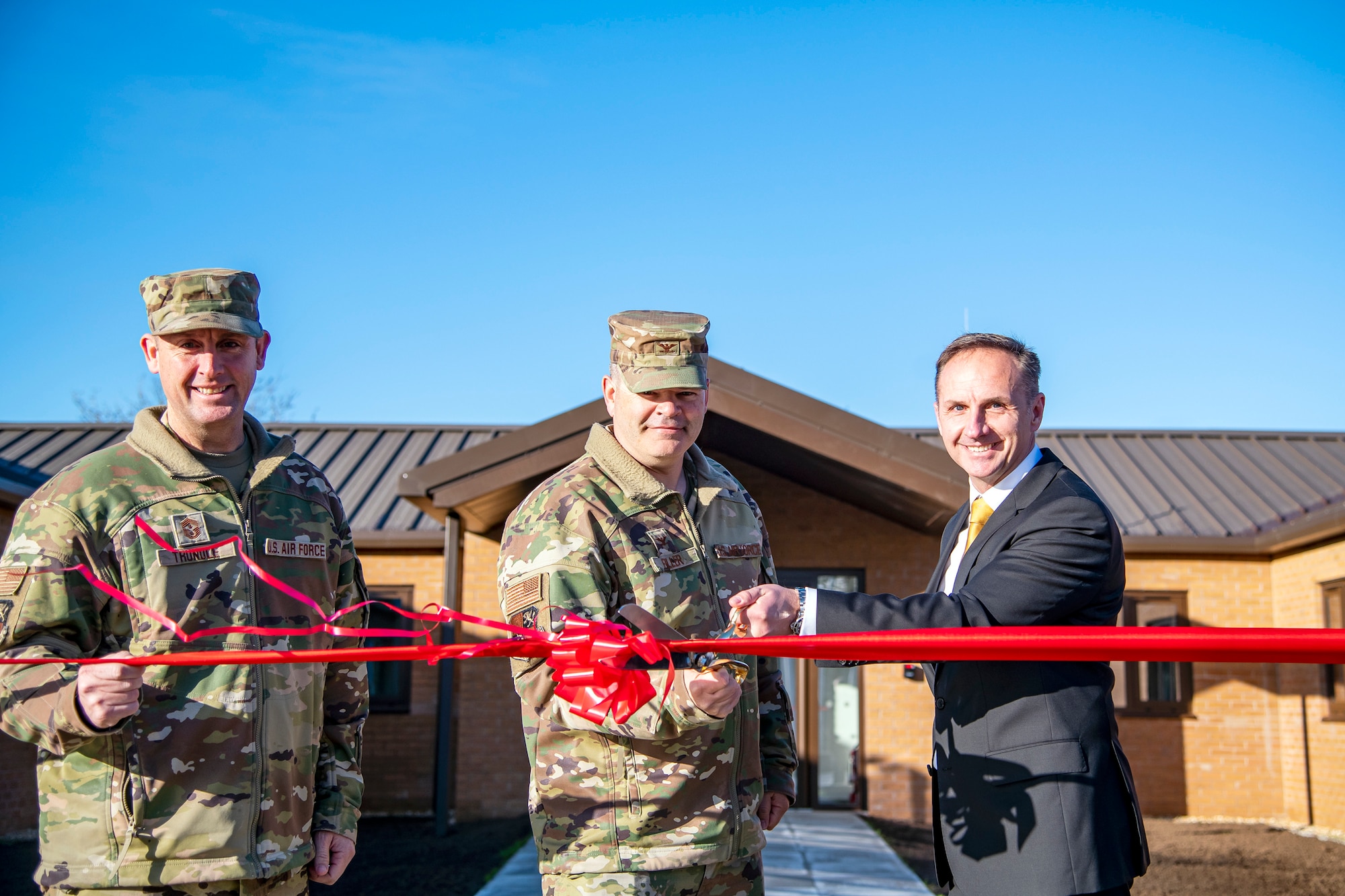 U.S. Air Force Col. Brian Filler, center, 501st Combat Support Wing commander, cuts a ribbon in front of the new 501st CSW headquarters building at RAF Fairford, England, Dec. 6, 2022. The Pathfinder command team marked the beginning of the headquarters transfer from RAF Alconbury to RAF Fairford. (U.S. Air Force photo by Staff Sgt. Eugene Oliver)