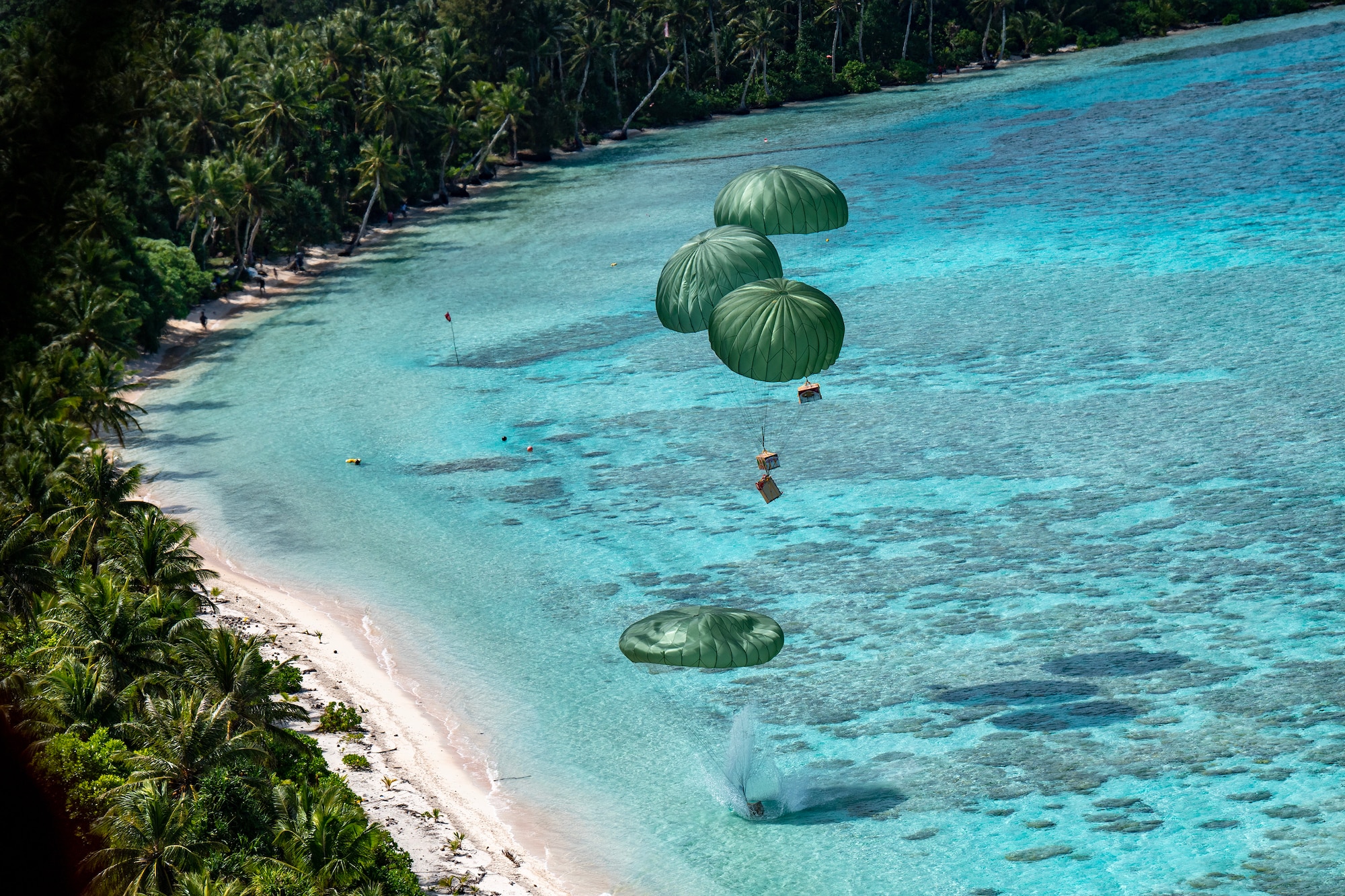 Four humanitarian aid bundles descend from a U.S. Air Force C-130J Super Hercules