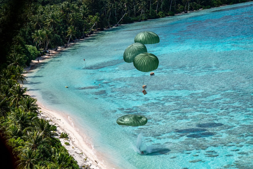 Boxes tied to parachutes land near the shore of an ocean.