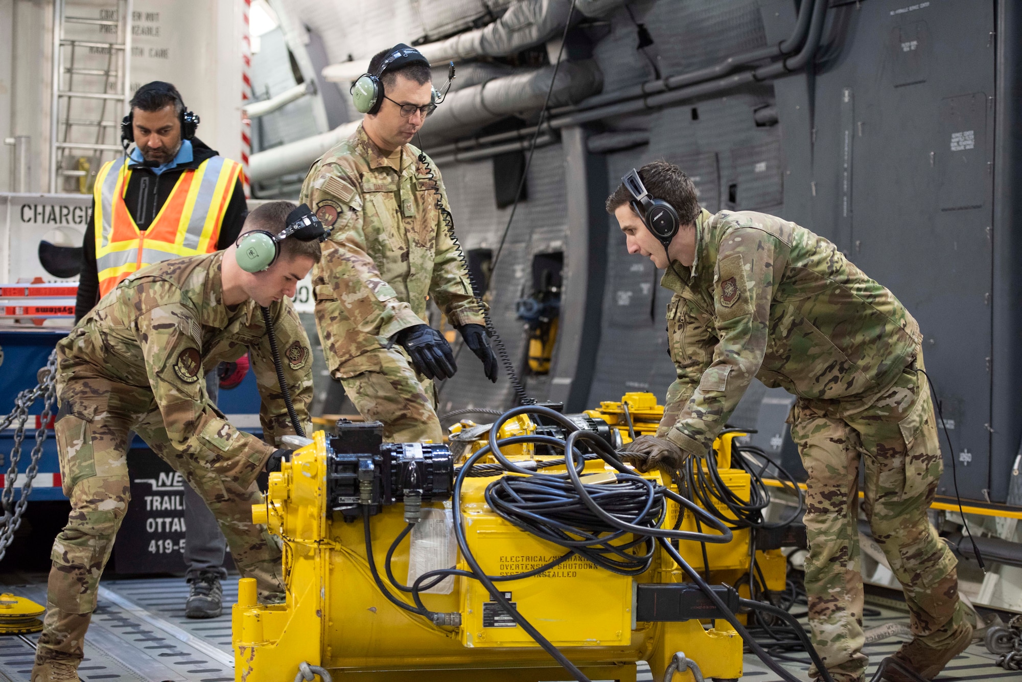 Airmen move a cargo winch inside an airplane.