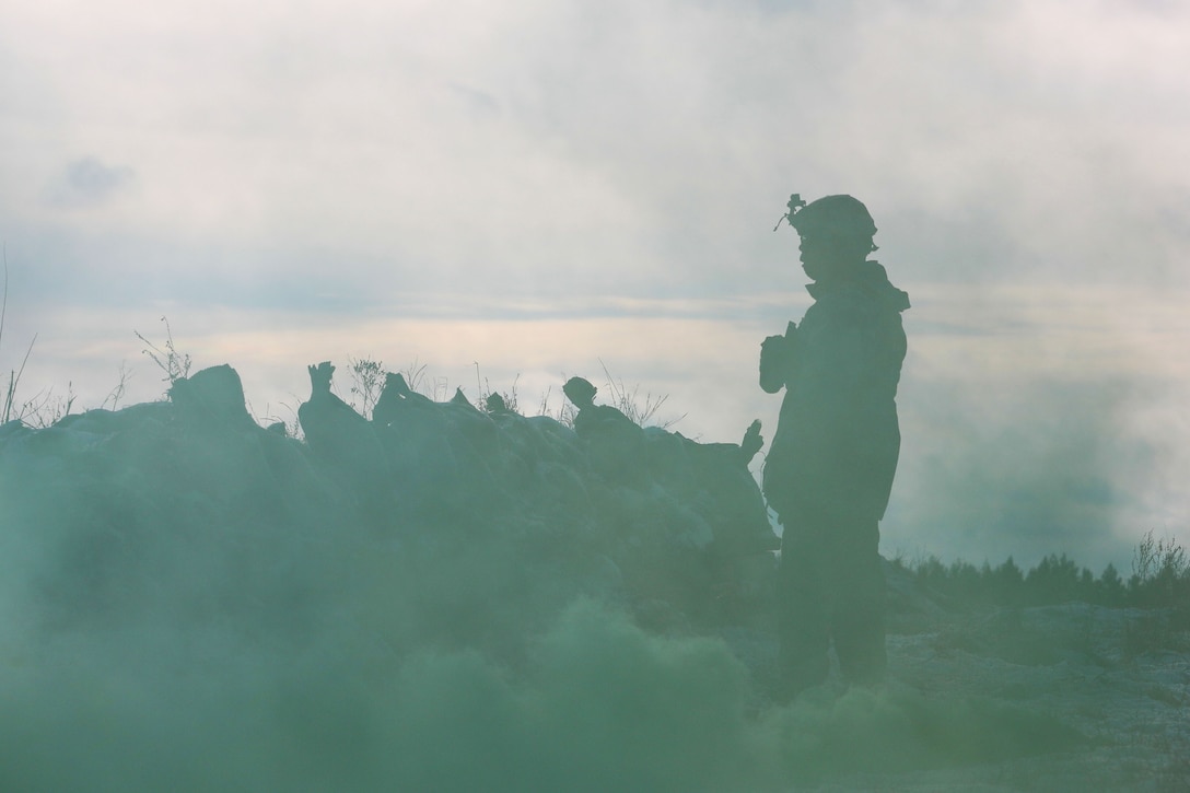 A soldier, shown in profile and silhouette, stands in a fog-shrouded field and looks into the distance.