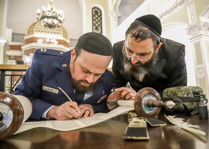 WARSAW, Poland - U.S. Air Force Capt. Levy Pekar, left, from Beitar, Israel, Chaplain of the 86th Airlift Wing based out of Ramstein Air Base, Germany, signs a Torah Scroll dedicated to the Ukrainian Army as Hillel Cohen, Military Rabbinate of Ukraine, watches during the ceremony, Nov. 29, 2022, Warsaw, Poland. Jewish Chaplains alongside distinguished guests, refugees from Ukraine, and U.S. ally partner nations attended the event to support the Ukrainian Chaplaincy’s religious support efforts. (U.S. Army photo by Spc. Devin Klecan)