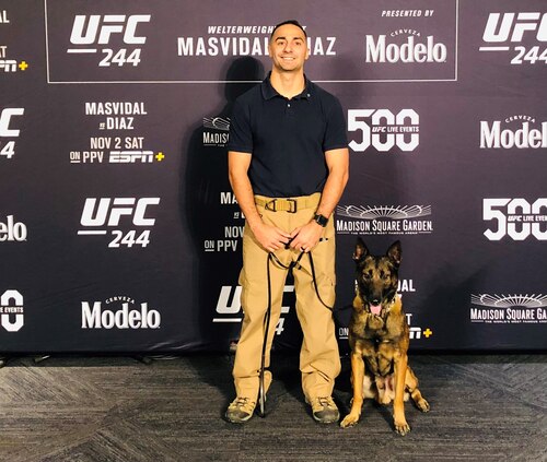 Photo shows man and dog posing in front of UFC backdrop.
