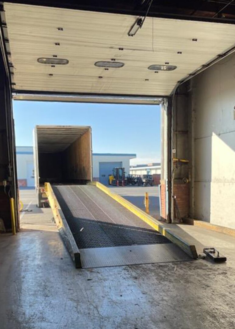 View of a portable loading ramp spanning the distance from a warehouse to a cargo truck. The ramp is open to the weather.