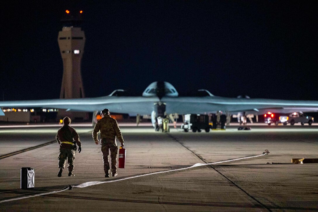 Two airmen walk toward an aircraft on a tarmac.