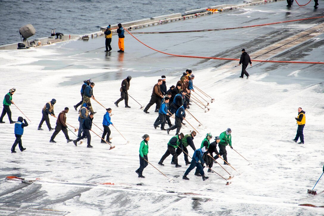 Sailors use brooms to wash the flight deck of a ship at sea.