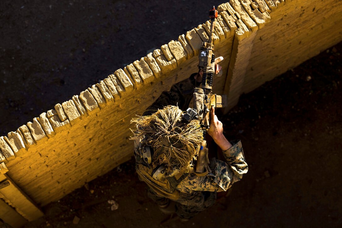 A Marine aims a weapon over a fence.