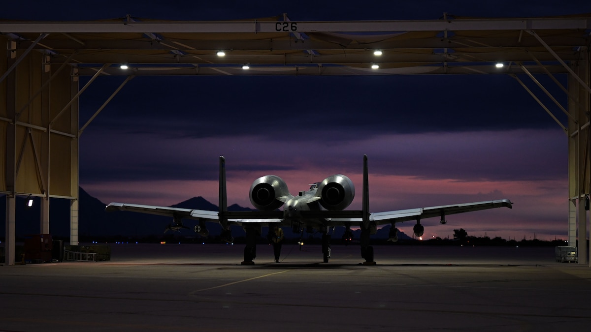 A photo of a military aircraft under on a flight line as the sun sets in the background.