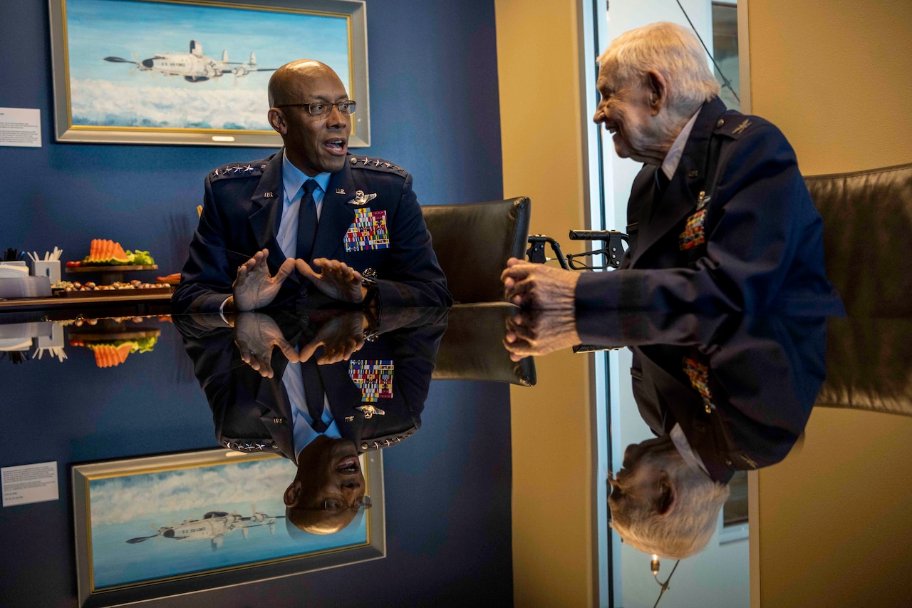 An airman and a World War II veteran sit at a table.