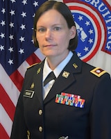 Woman in U.S. Army uniform, standing in front of two flags.