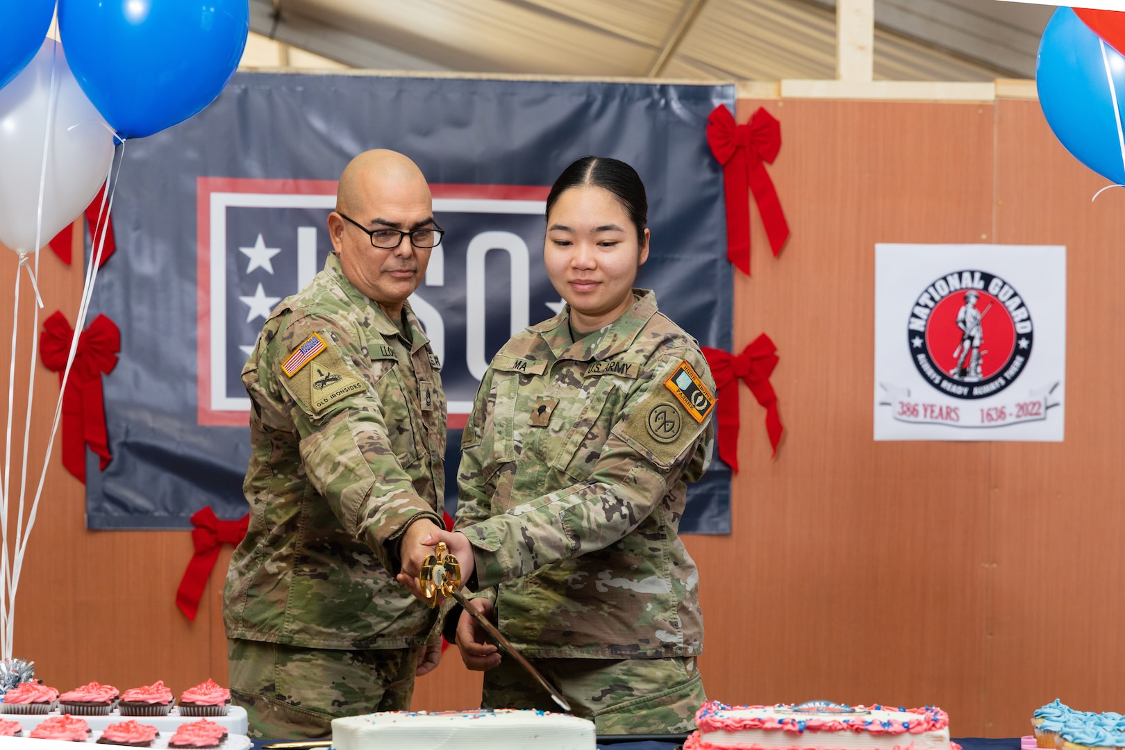 U.S. Army Sgt. 1st Class Raul Llopis, a unit supply specialist, and Spc. Catherina Ma, a combat medic, both assigned to Task Force Orion, 27th Infantry Brigade Combat Team, New York Army National Guard, carry on the Army tradition of a unit’s oldest and youngest Soldiers cutting a cake during a celebration of the 386th National Guard birthday in Grafenwohr, Germany, Dec. 13, 2022. The formation of the first militia regiments in North America Dec. 13, 1636, is recognized as the birth of the National Guard.