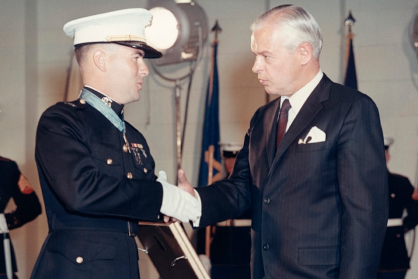 A man shakes the hand of a man holding a plaque.