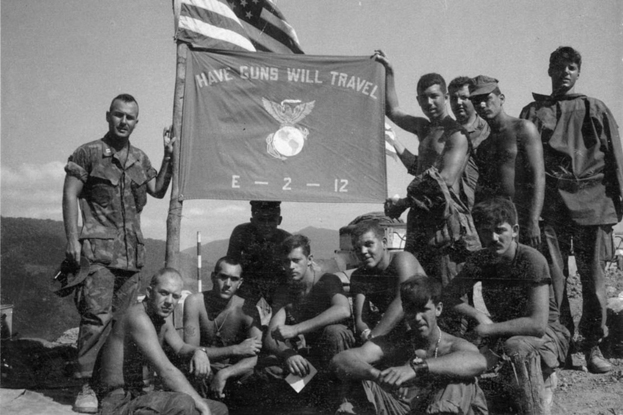 Several men pose for a photo while holding a unit flag that flies under an American flag.