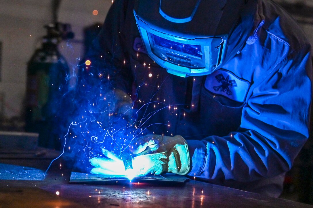 A person wearing protective gear welds equipment as sparks fly.