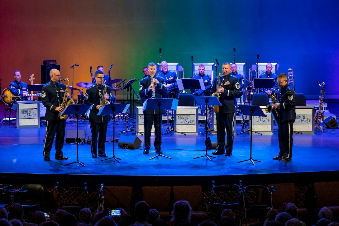 Musicians play brass instruments on a stage in front of an audience.