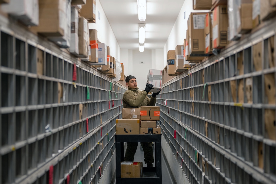 A person stands next to a rack of mail slots and holds a taped box.