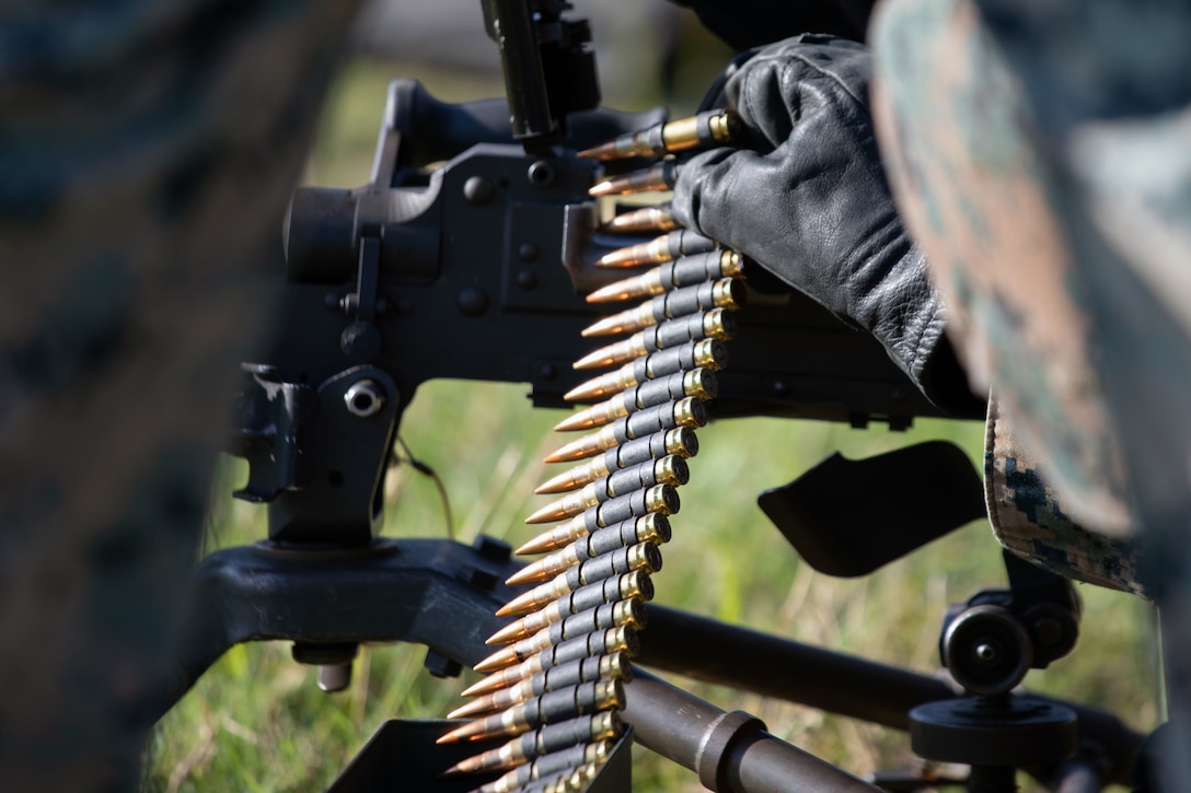 A Marine holds an ammunition belt next to a weapon.