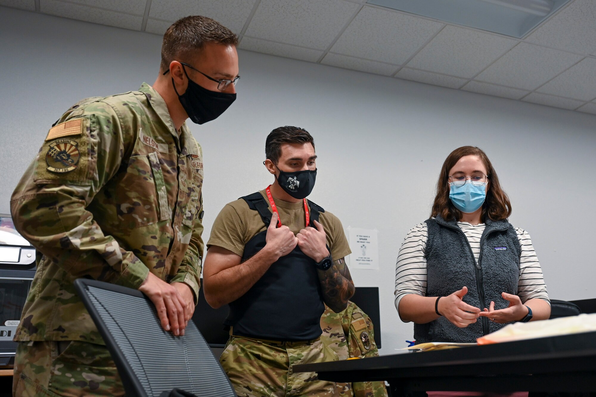 A photo of three people looking at a prototype of a vest placed on a table.