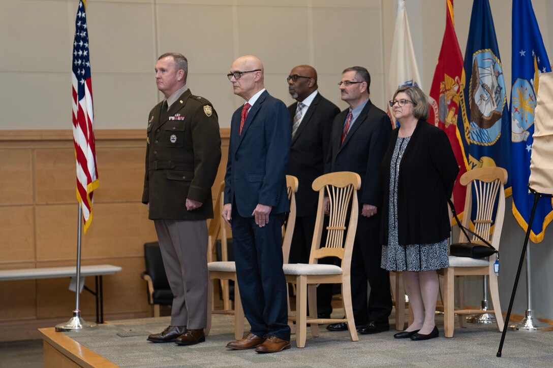 military man, civilian men and woman stand together on stage