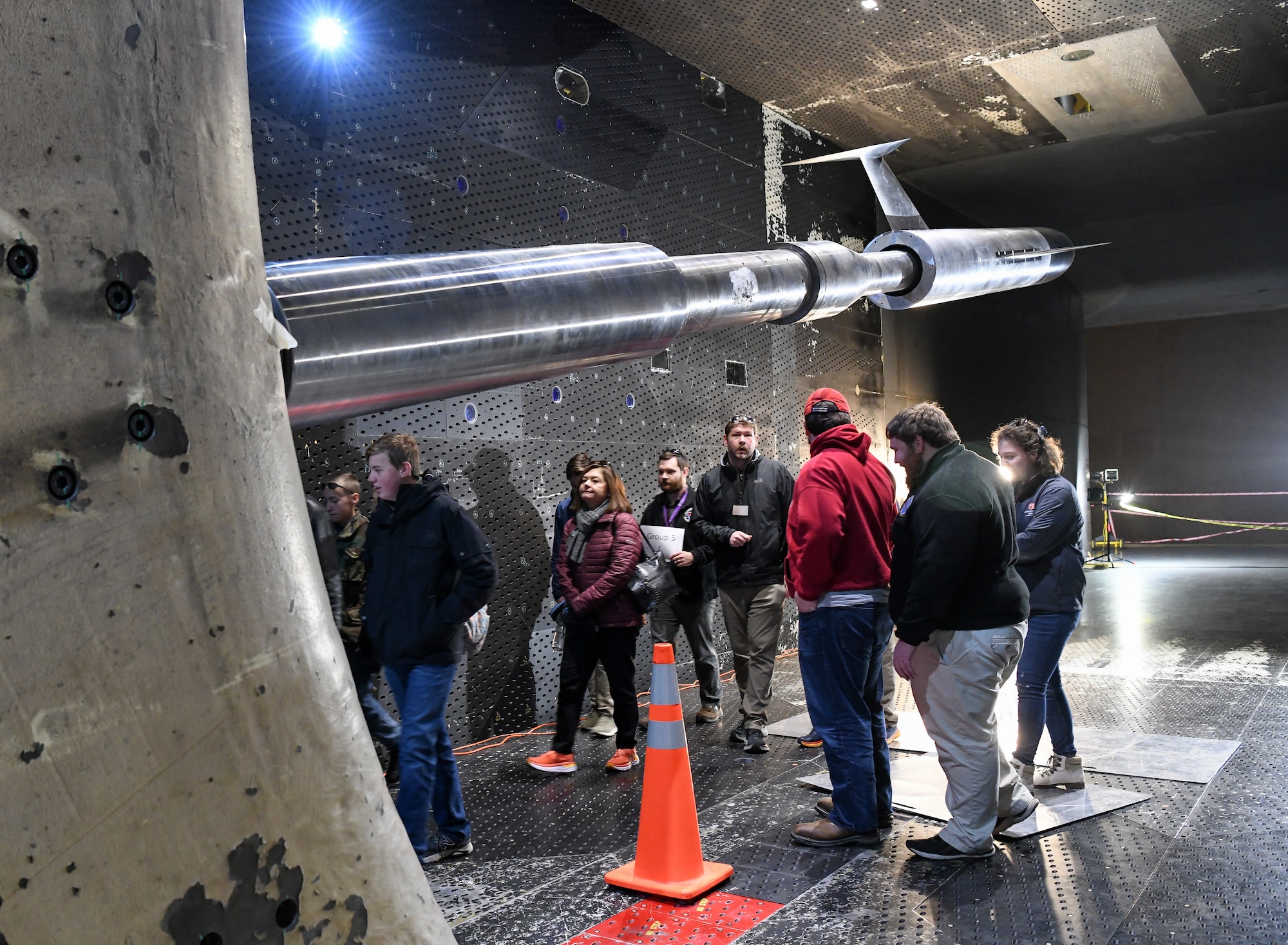 Group of people walking underneath a test model inside a wind tunnel