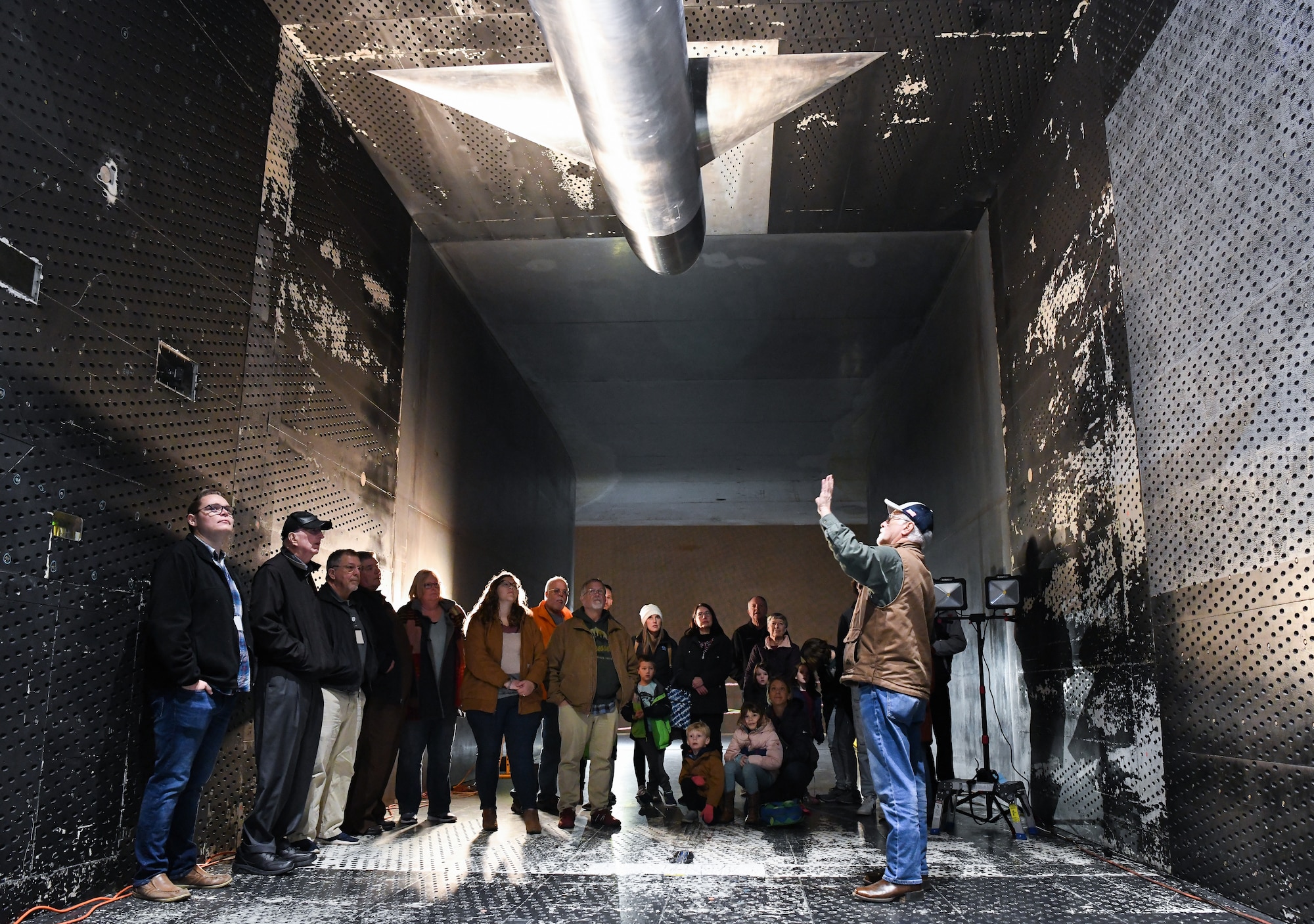 Man speaking to group of people standing inside a wind tunnel