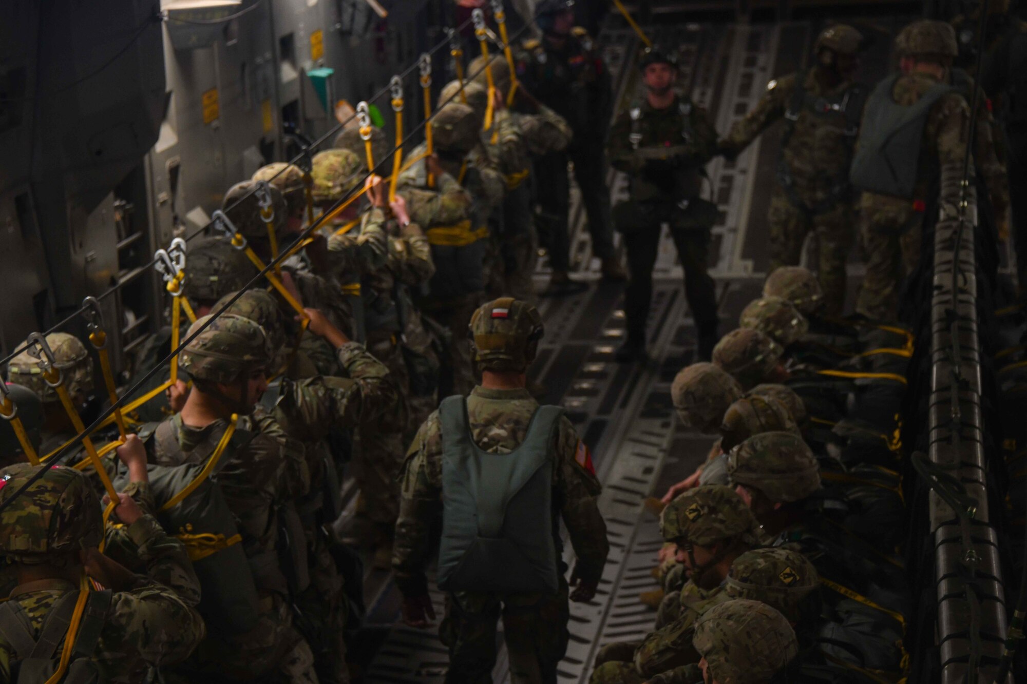 A U.S. Army soldier wearing a Poland flag on his helmet walks down a line of jumpers to prepare them for their drop over the Sicily Drop Zone near Fayetteville, North Carolina, Dec. 8, 2022. Many of the soldiers from the U.S. Army traded their U.S. flag patches to their partner nation jumpers in return for that country’s flag patch. (U.S. Air Force photo by Airman 1st Class Kari Degraffenreed)
