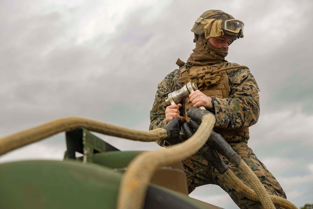 A Marine attaches a hose to a water trailer.