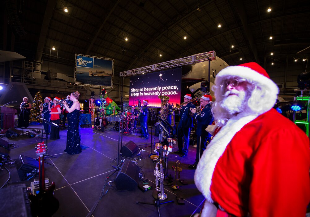 Santa stands in the foreground on the wing of the stage as the band plays in the background.