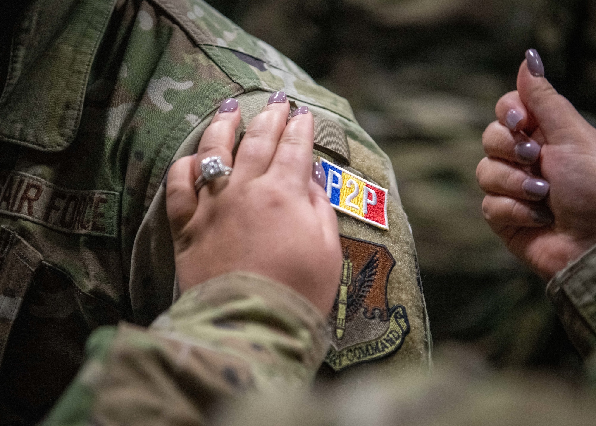 An Airman attaches a peer support identification tab onto the shoulder of another Airman.