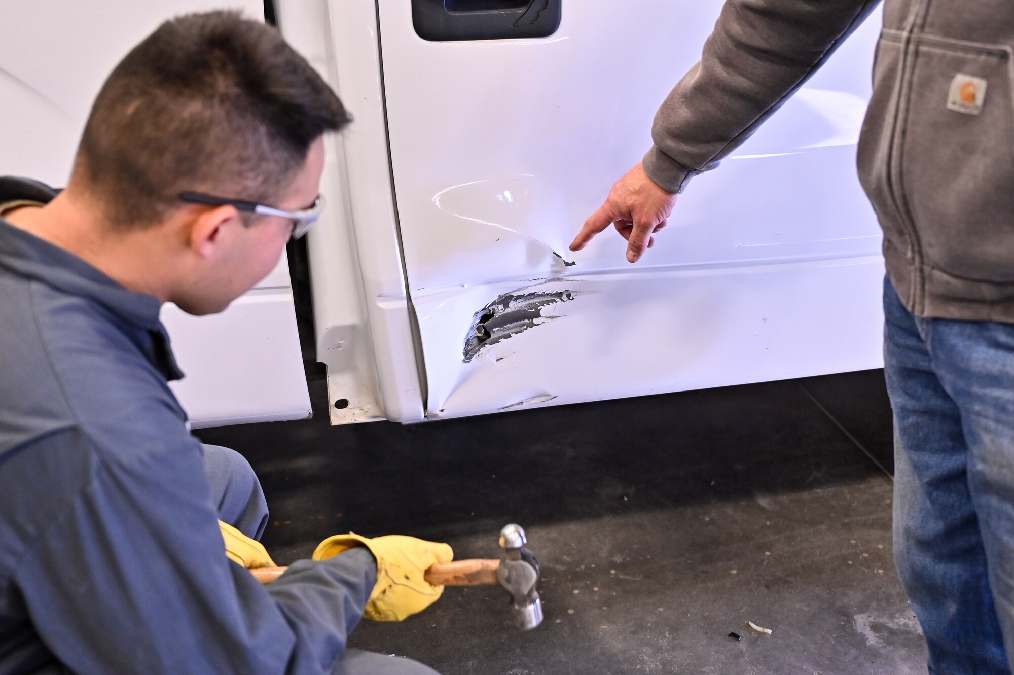 Thomas Hoadley, 90th Logistics Readiness Squadron mobile metal mechanic, shows Airman 1st Class Marcos Orellana, 90 LRS vehicle maintenance technician, the damage on a Ford truck and discusses the actions they will take to repair it on F.E. Warren Air Force Base, Wyoming, Nov. 29, 2022. With more than 40 years of experience, the 90 LRS Monster Garage or body shop team is repairing the 90th Missile Wing fleet while supporting the Air Force Global Strike priority of people by finding ways to train the next generation of Airmen and find innovative solutions. (U.S. Air Force photo by Joseph Coslett Jr.)