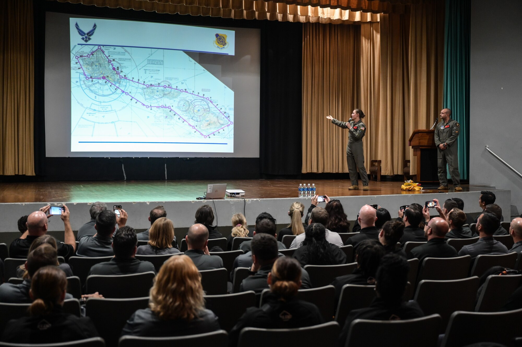Capt. Carol Champion, 535th Airlift Squadron C-17 Globemaster III pilot, and Senior Master Sgt. Paul Garcia, 535th AS senior enlisted leader, give a mission brief to Executive Leadership Development Program participants in the Hickam Theater at Joint Base Pearl Harbor-Hickam, Hawaii, Dec. 6, 2022. The ELDP participants flew on a C-17 for a two-hour sortie over the Hawaiian Islands. (U.S. Air Force photo by Staff Sgt. Alan Ricker)
