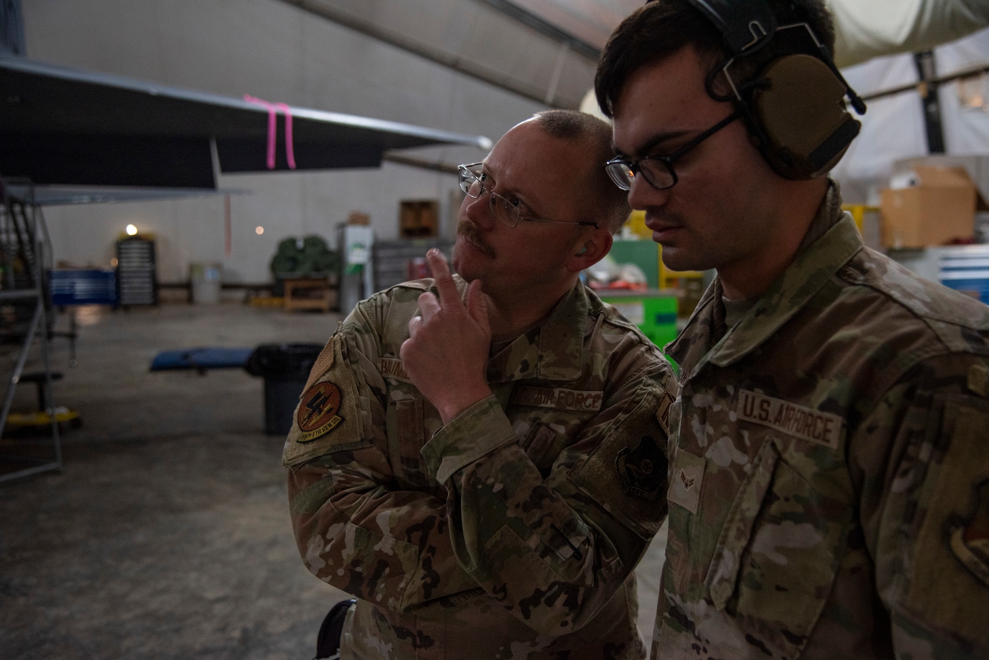 Master Sgt. David Baumberger, 389th Expeditionary Fighter Generation Squadron, Specialist Section Chief (left), speaks with Senior Airman Elijah Gardner, 332d Expeditionary Civil Engineer Programs specialist. Gardner is participating in "Maintainer for a Day" at an undisclosed location, Southwest Asia, Nov. 25, 2022. "Maintainer for a Day" is a program that allows Airmen from diverse career fields to experience what it’s like to perform maintenance and repair work on an aircraft. (U.S. Air Force photo by: Tech. Sgt. Jim Bentley)