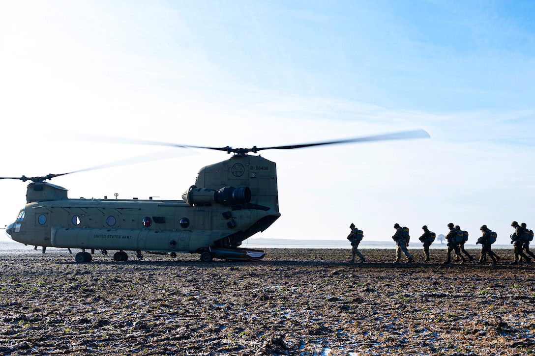 Service members walk towards a helicopter.