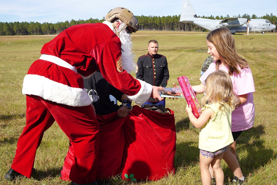 Marine dressed as Santa hands gifts to girls during a Toys for Tots event.