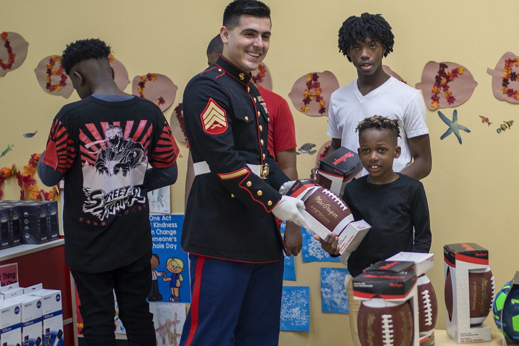 Smiling Marine hands football to boy at Toys for Tots event.