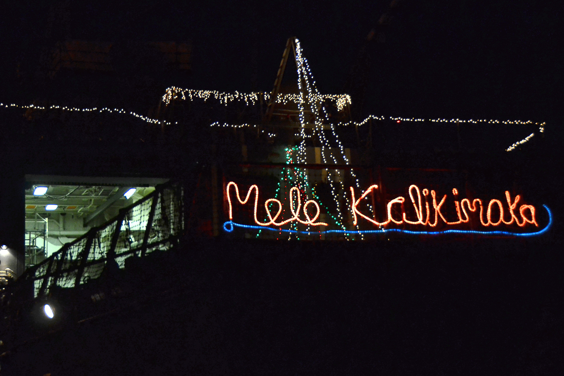 U.S. Navy ship is decorated with holiday lights with the Hawaiian phrase 