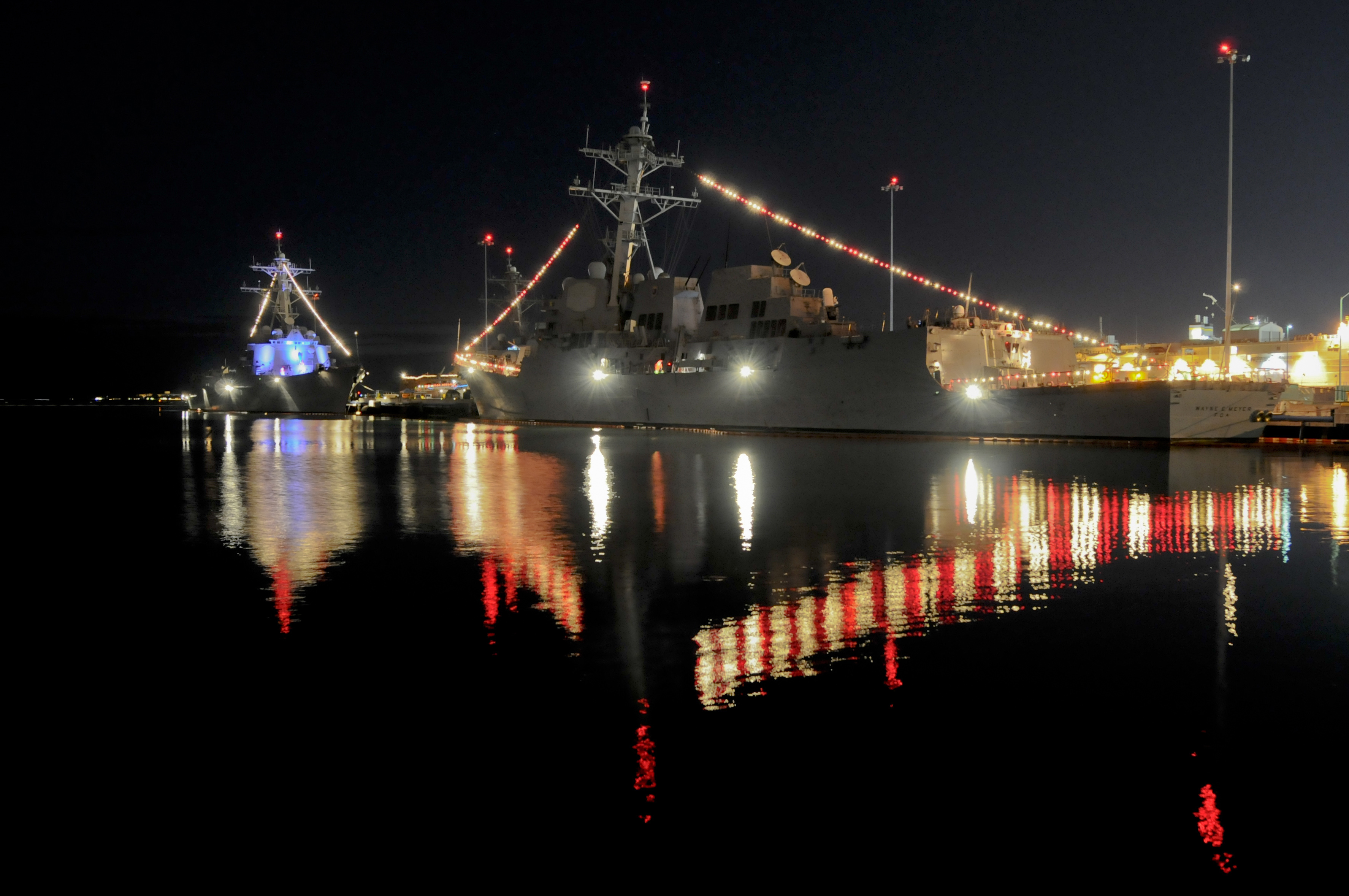 Two U.S. Navy ships are shown illuminated with holiday lights.