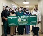 1st Lt. Maria Frisone, center, a nurse at Walter Reed National Military Medical Center (WRNMMC), is presented a commerative DAISY Award honoree banner at WRNMMC in Bethesda, Maryland. Frisone was nominated for The DAISY Award by a WRNMMC patient for professionalism, compassion, and attention to detail.