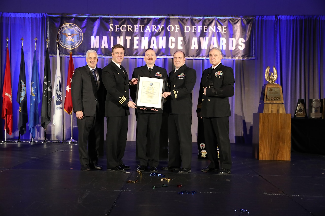 Five people stand for a photo while holding a certificate on a stage.