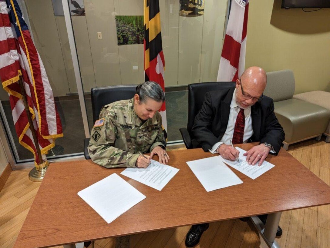 Two people sitting down to sign a sheet of paper.
