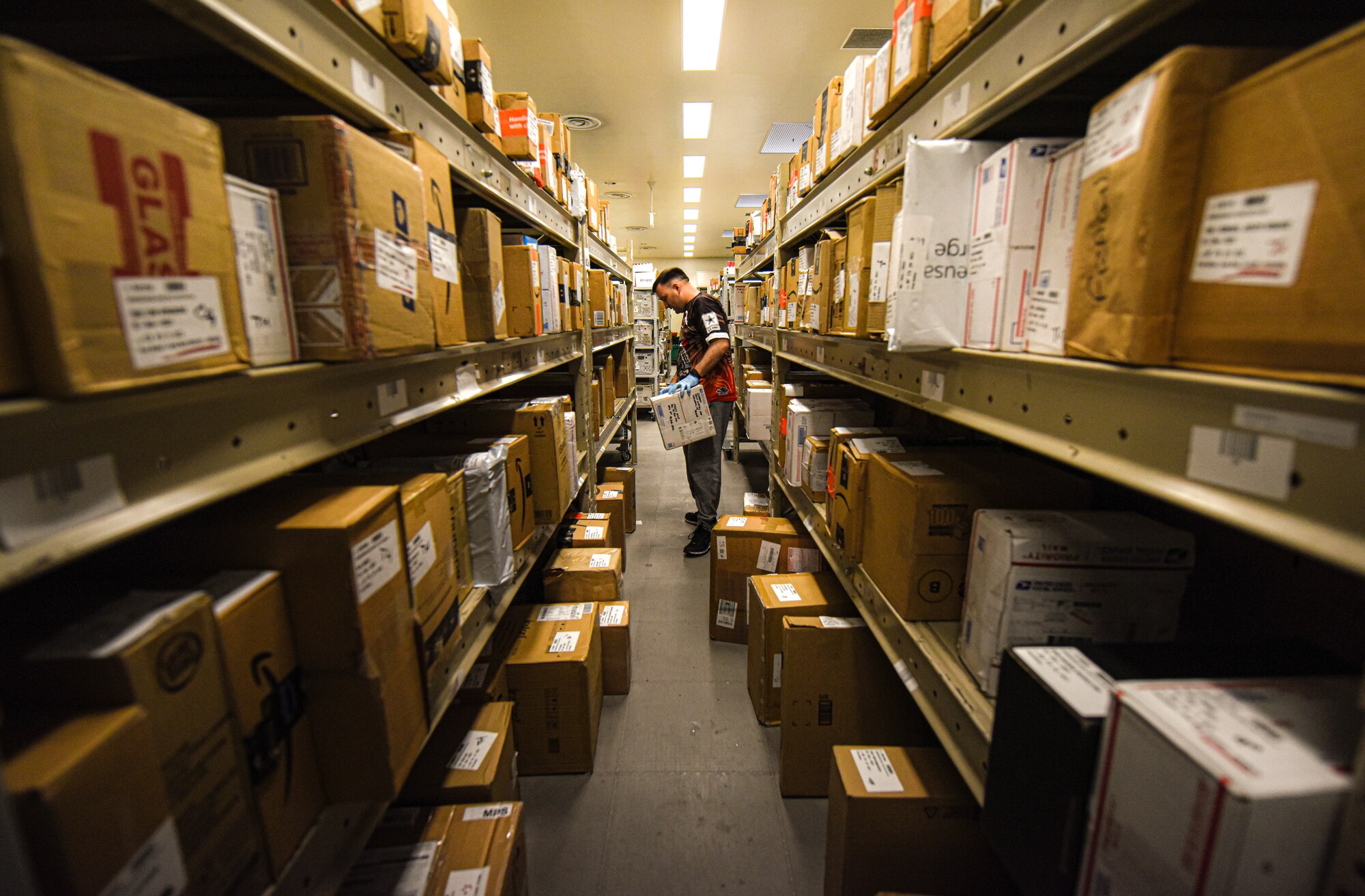 1st Sgt stands in between rows of packages holding a package in hand and locating another