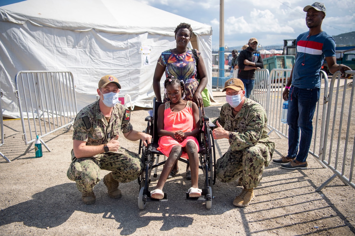 Capt. Michael Weaver, right, ground force commander for Continuing Promise 2022 in Haiti, and Lt. j.g. Blake Dunn, an intensive care unit nurse from Atlanta, Georgia, assigned to the hospital ship USNS Comfort (T-AH 20), give a wheelchair to a young Haitian after providing care at a medical site in Jeremie, Haiti, Dec. 12, 2022. Comfort is deployed to U.S. 4th Fleet in support of CP22, a humanitarian assistance and goodwill mission conducting direct medical care, expeditionary veterinary care, and subject matter expert exchanges with five partner nations in the Caribbean, Central and South America. (U.S. Navy photo by Mass Communication Specialist 1st Class Benjamin Lewis)