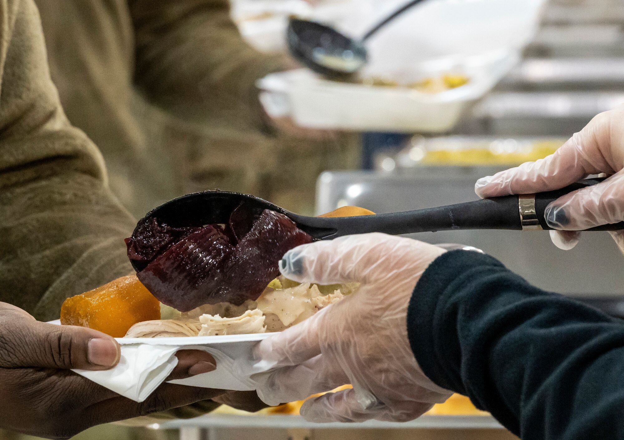 A volunteer serves cranberry sauce to a Team Dover Airman during Operation Feed the Troops on Dover Air Force Base, Delaware, Dec. 14, 2022. OFT volunteers served a traditional holiday meal to members of Team Dover during lunch and dinner meal times. Seventy turkeys were prepared and donated by local businesses for the event. (U.S. Air Force photo by Senior Airman Stephani Barge)