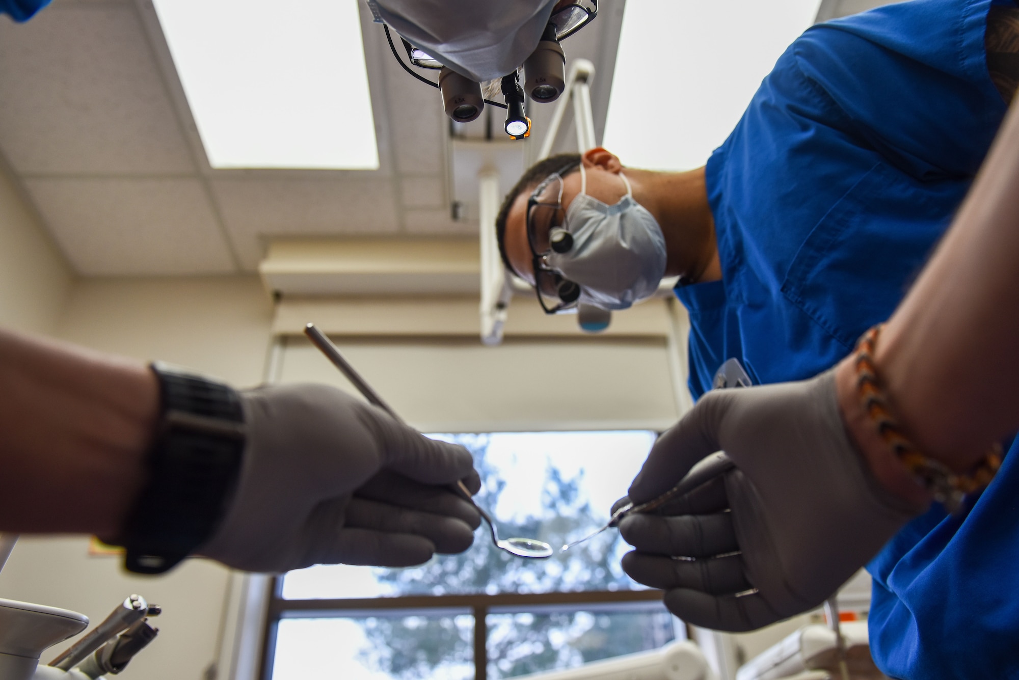 Dr. (Capt.) Clifton Wright (top), 8th Operational Medical Readiness Squadron general dentist, prepares for a procedure as Senior Airman Malik Veveiros, 8th OMRS dental technician, observes at Kunsan Air Base, Republic of Korea, Dec. 14, 2022. Dentists use a variety of equipment to include mirrors, lights and magnifiers to help them see inside a patient’s mouth. (U.S. Air Force Photo by Tech. Sgt. Timothy Dischinat)