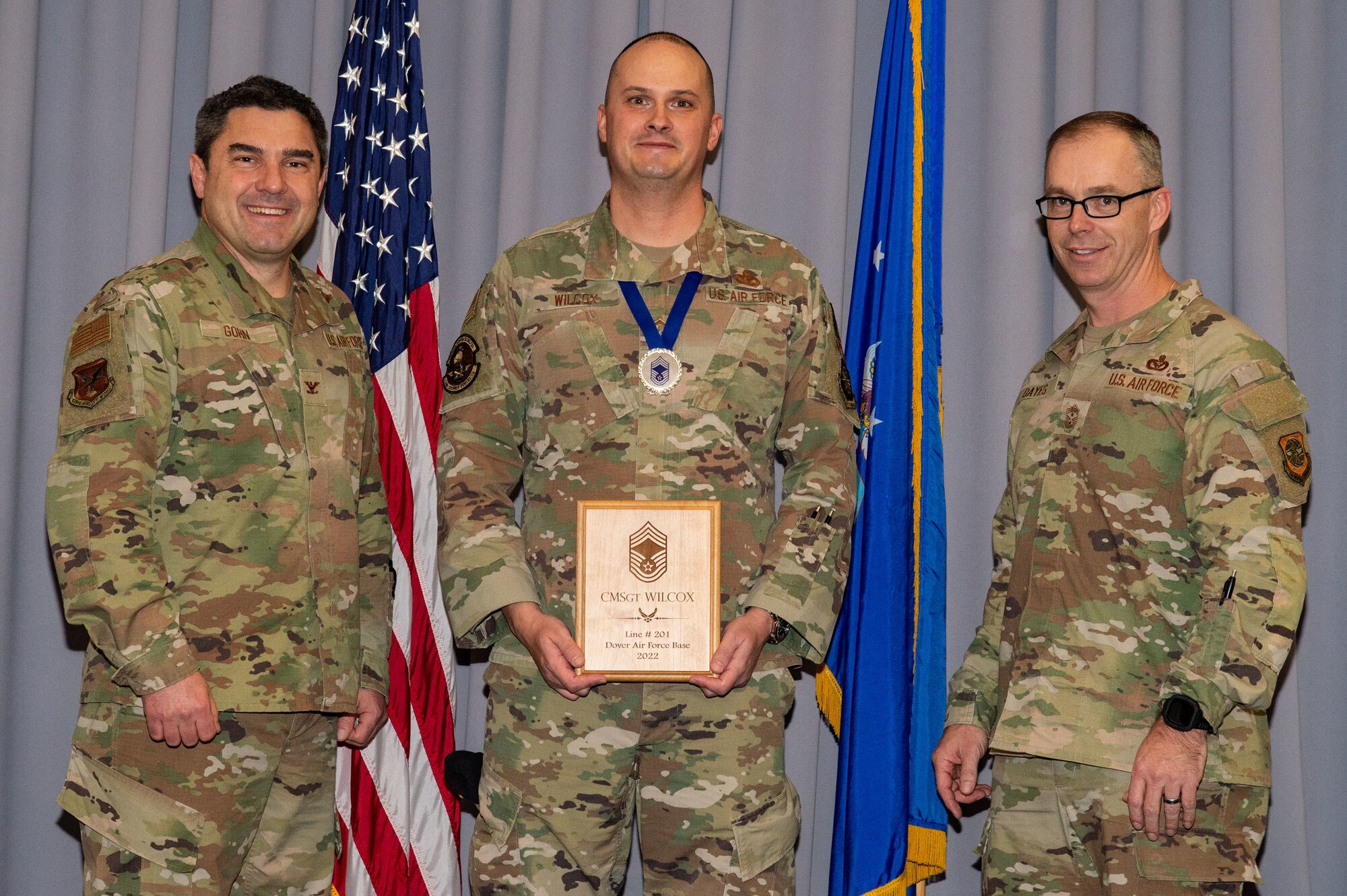 Col. Rusty Gohn, left, 436th Airlift Wing vice commander, and Chief Master Sgt. Timothy Bayes, right, 436th AW command chief, present Chief Master Sgt.-select Paul Wilcox, 436th Security Forces Squadron operations superintendent, with a plaque noting his promotion to chief at The Landings on Dover Air Force Base, Delaware, Dec. 8, 2022. Senior Master Sgt. Wilcox was one of 514 Airmen selected for promotion to the top enlisted rank of chief. (U.S. Air Force photo by Roland Balik)