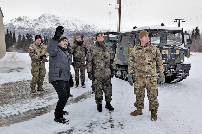 Service members stand in the snow next to a person pointing up to the sky.