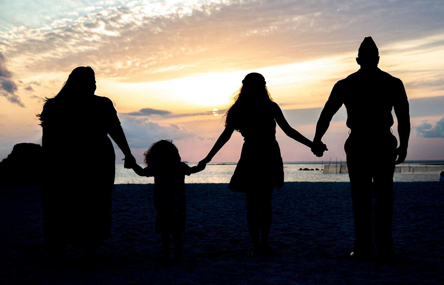 A military family watches a sunset on the beach.