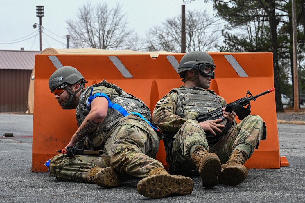 Two Airmen take cover behind an orange barricade.