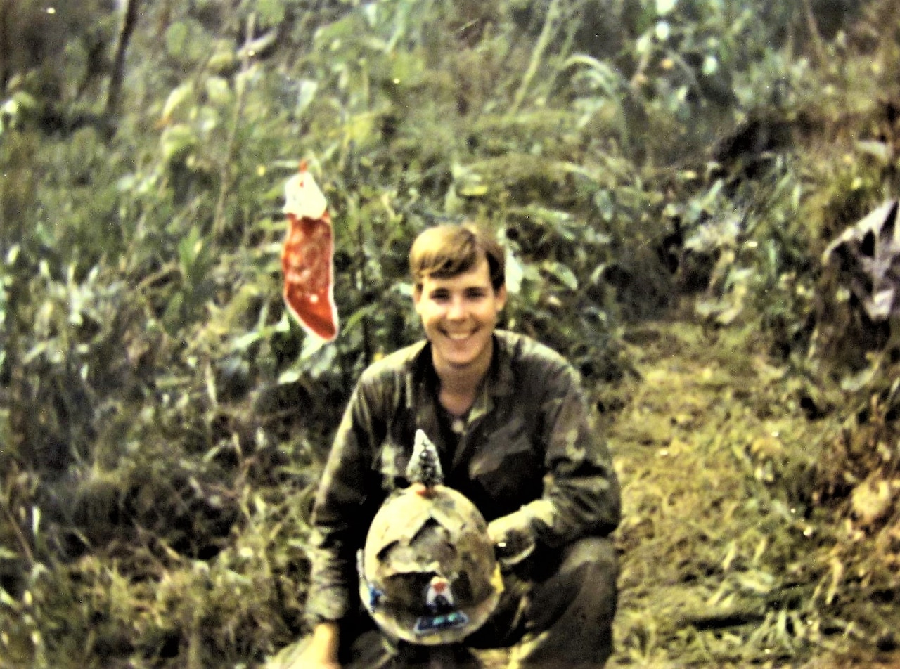 A Marine bent on one knee with a helmet in his hand, poses for a photo.