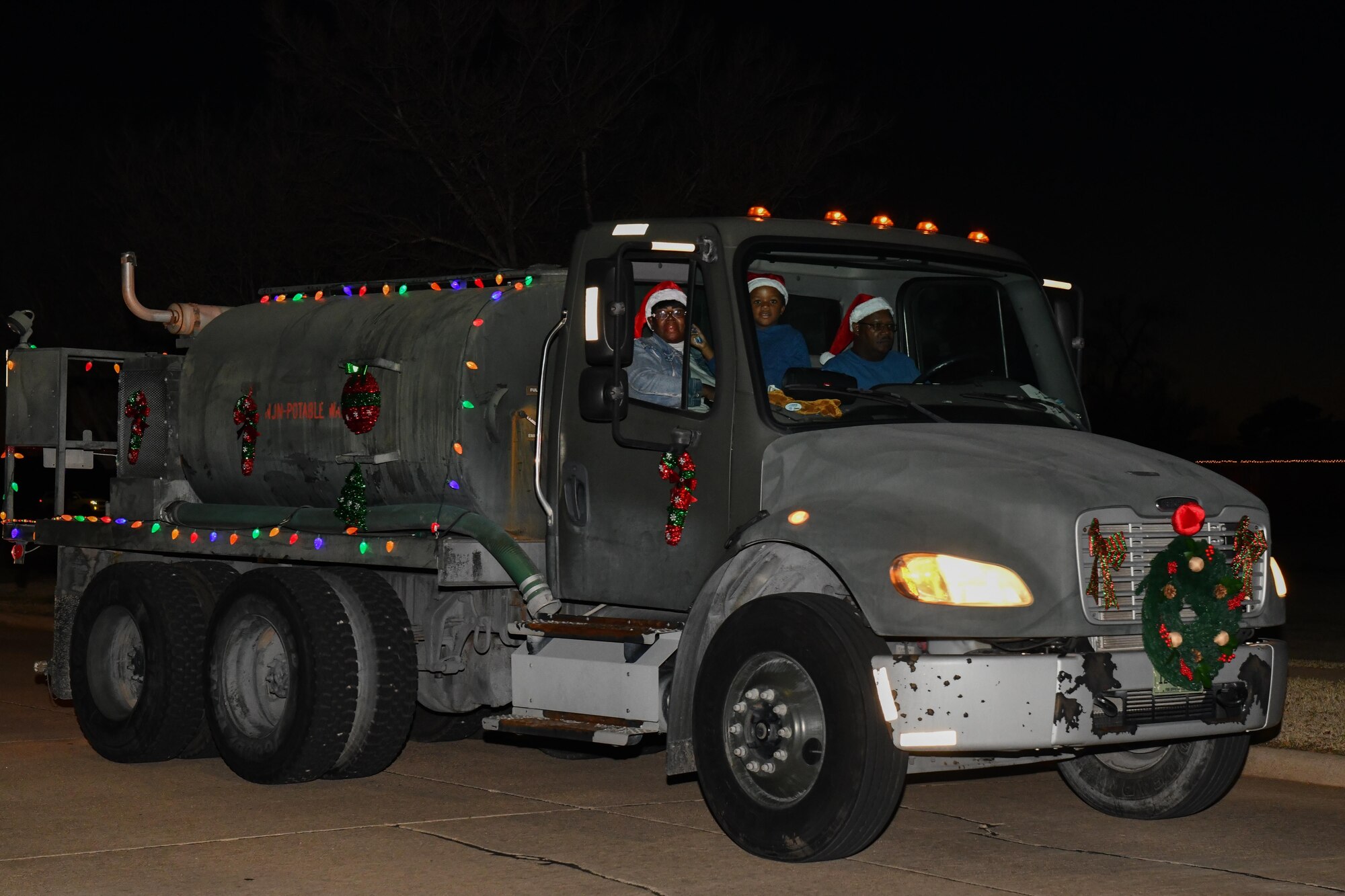 Donald Johnson, 97th Civil Engineer Squadron crane operator, and his wife and grandson, Jerri and Jahbari, drive a tanker truck during a holiday parade at Altus Air Force Base, Oklahoma, Dec. 13, 2022. This is Altus Air Force Base’s third annual holiday parade and was hosted by the 97th Civil Engineer Squadron. (U.S. Air Force photo by Airman 1st Class Miyah Gray)